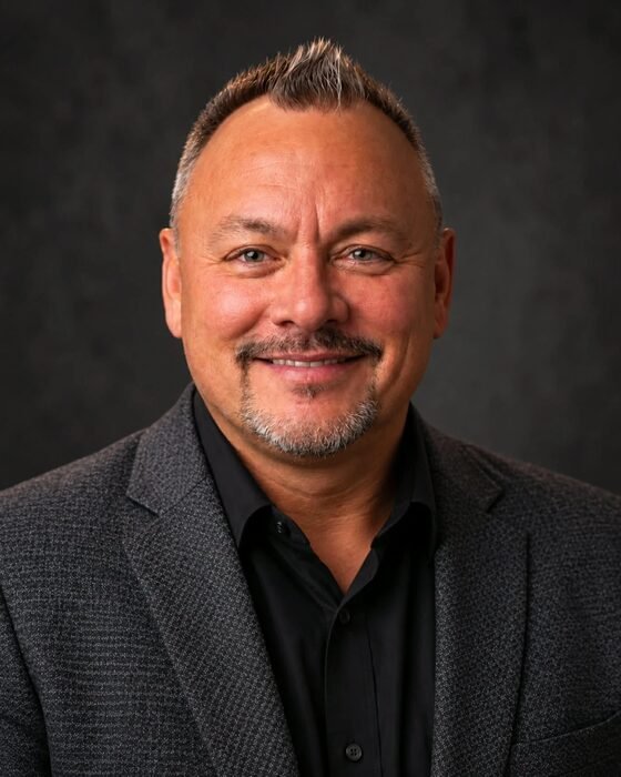 Nate Hall, smiling, in a charcoal blazer and black shirt